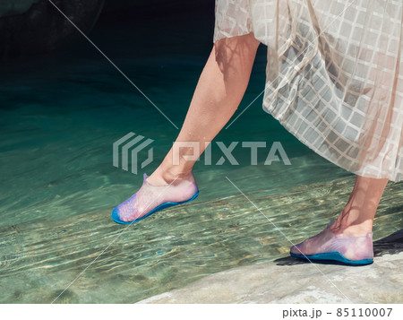 Woman's wet feet taking a step into clear turquoise water outdoors in sun light Woman's wet feet taking a step into clear turquoise water outdoors in sun light 85110007
