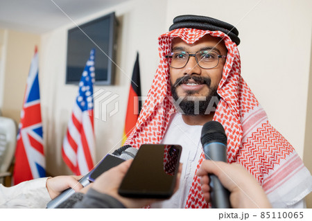 Young confident delegate in national clothes speaking in microphone held by journalist Young confident delegate in national clothes speaking in microphone held by journalist 85110065