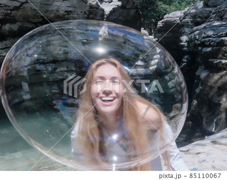 Laughing girl looks through a huge shiny soap bubble surrounded by rocky nature on a sunny day Laughing girl looks through a huge shiny soap bubble surrounded by rocky nature on a sunny day 85110067