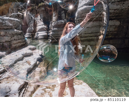 The girl blows huge soap bubbles into the canyon gorge near the clear river. View through the bubble 85110119
