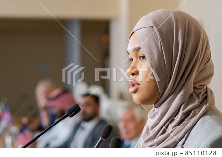 Young pretty female speaker in hijab talking to audience at conference 85110128
