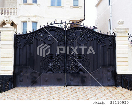 Black gates with a wrought-iron pattern of monograms adjoin the white columns of the fence that encloses a private villa 85110939