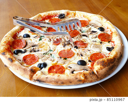 Freshly baked pizza with mushrooms, sausage and olives stands on a wooden table. Closeup photo Freshly baked pizza with mushrooms, sausage and olives stands on a wooden table. Closeup photo 85110967