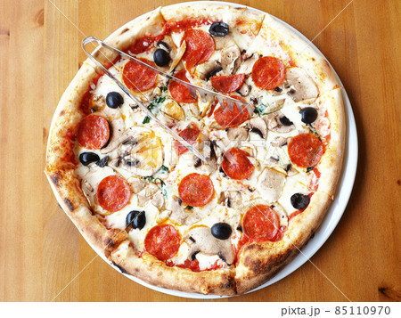 Fresh pizza with mushrooms, sausage and olives stands on a wooden table. Top view 85110970