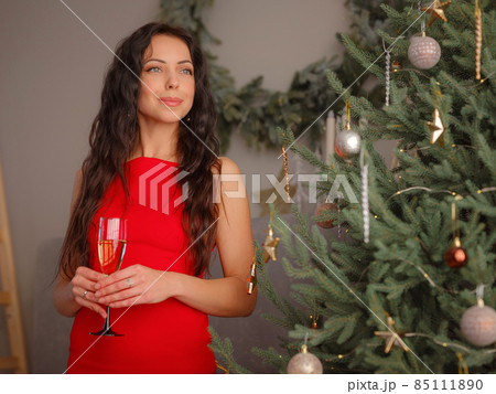 smiling woman in evening dress with glass of sparkling wine over christmas tree lights background 85111890