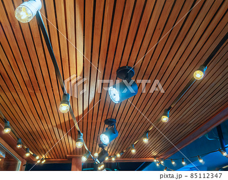 Spotlights and bulbs hang on a metal frame under a wooden canopy Spotlights and bulbs hang on a metal frame under a wooden canopy 85112347
