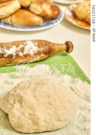 Raw dough and rolling pin near homemade pies in kitchen 85113581