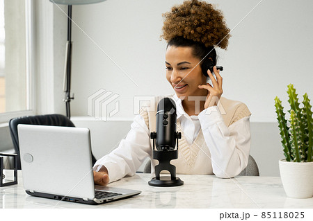 Young black woman is making an online podcast recording for her online show. An attractive African-American business woman speaking into a microphone for a radio program. 85118025