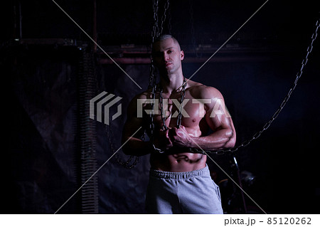 Young shirtless muscular man standing among metal chains, looking at camera, copy space 85120262