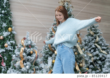 New Year portrait of beautiful smiling caucasian young woman in cozy wool warm light blue sweater standing near decorated Christmas tree. happy person New Year portrait of beautiful smiling caucasian young woman in cozy wool warm light blue sweater standing near decorated Christmas tree. happy person 85120417