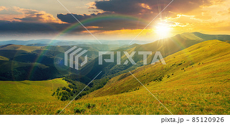 mountain landscape in summer at sunset. grassy meadows on the hills rolling in to the distant peak beneath a rainbow in evening light mountain landscape in summer at sunset. grassy meadows on the hills rolling in to the distant peak beneath a rainbow in evening light 85120926