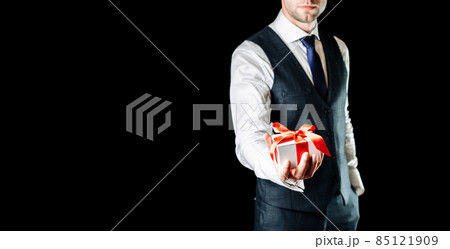 Gift man. Happy young businessman holding surprise gift box present with red ribbon isolated on black background. Black Friday, Valentine Day congratulations banner. 85121909