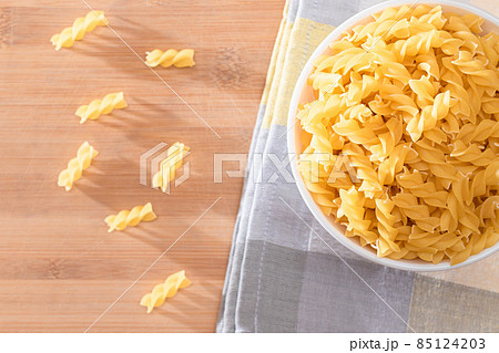 Uncooked Fusilli Pasta in White Bowl on Wooden Board 85124203