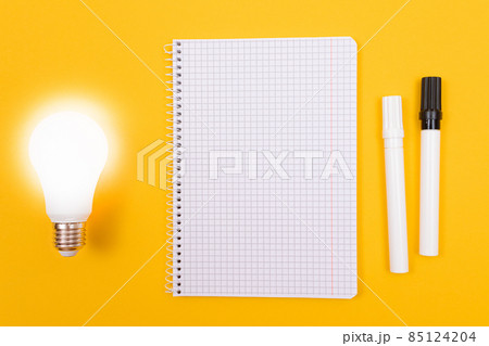 Glowing Power Saving Lamp with Notepad Lying on Yellow Table Glowing Power Saving Lamp with Notepad Lying on Yellow Table 85124204