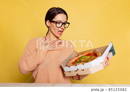 Young surprised girl holding box with pizza isolated on yellow studio background. World pizza day 85125082