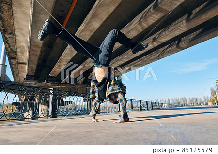 Young man break dancer dancing on urban background performing acrobatic stunts Young man break dancer dancing on urban background performing acrobatic stunts 85125679