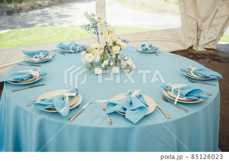 Wedding tables for guests. Round tables with a blue tablecloth. Decorated with flowers, plates, glasses and more Wedding tables for guests. Round tables with a blue tablecloth. Decorated with flowers, plates, glasses and more 85126023