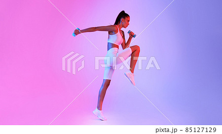 Determined Fitness Lady Jumping Exercising Holding Dumbbells Over Neon Background Determined Fitness Lady Jumping Exercising Holding Dumbbells Over Neon Background 85127129