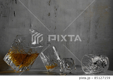 Glass of the whiskey with a square decanter on a grey clay textured background. Glass of the whiskey with a square decanter on a grey clay textured background. 85127159