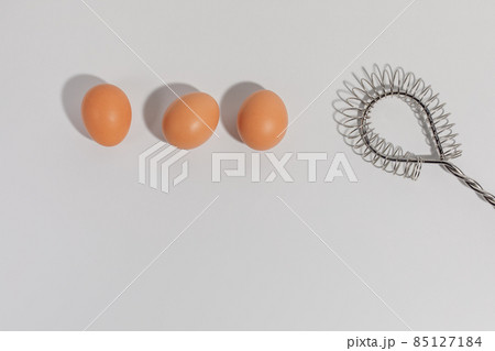 Three eggs and stainless steel Wire Whisk on white background 85127184