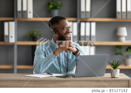Satisfied millennial black bearded man in glasses and headphones works at laptop and looks at empty space Satisfied millennial black bearded man in glasses and headphones works at laptop and looks at empty space 85127192