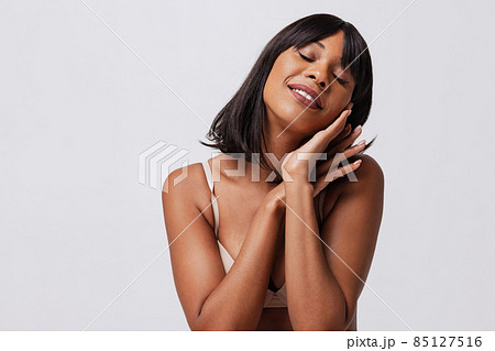 Half-length portrait of pretty dark skinned girl in white bra posing isolated over gray studio background. Natural beauty concept. Half-length portrait of pretty dark skinned girl in white bra posing isolated over gray studio background. Natural beauty concept. 85127516