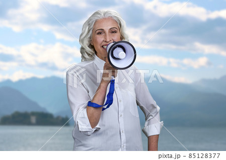 Portrait of beautiful senior lady wearing classic blouse talking into megaphone. Portrait of beautiful senior lady wearing classic blouse talking into megaphone. 85128377
