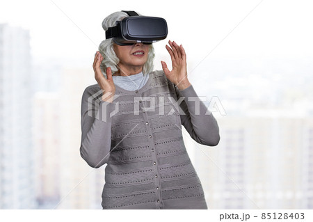 Surprised senior caucasian woman wearing virtual reality glasses on blurred background. 85128403
