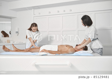 Women chiropractics in uniforms work with mature male patient lying on couch in spa salon 85129481