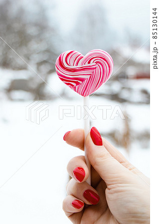 Hand holds pink lollipop. Sweet heart, symbol of valentines day. Cute gift in hands. 85130144