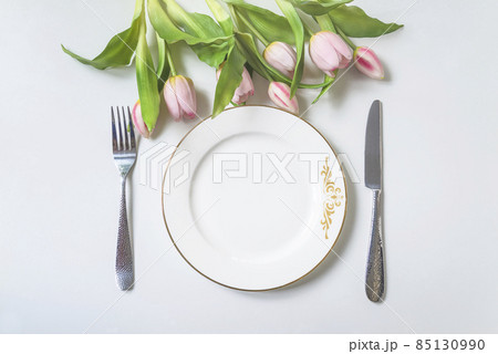 Spring holiday place setting; Top view of white plate, fork and knife and bouquet of pink tulips above 85130990
