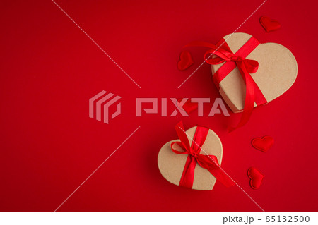 Two wrapped gift boxes in heart shape on red background, Saint Valentine Day 85132500