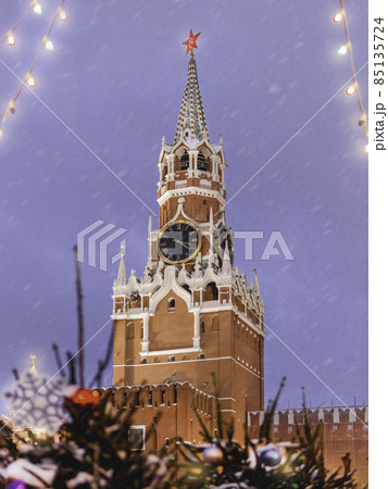 Spasskaya tower of Kremlin, view through light bulbs and Christmas trees. Traditional New Year fair on Red square in Moscow. Russia. Spasskaya tower of Kremlin, view through light bulbs and Christmas trees. Traditional New Year fair on Red square in Moscow. Russia. 85135724