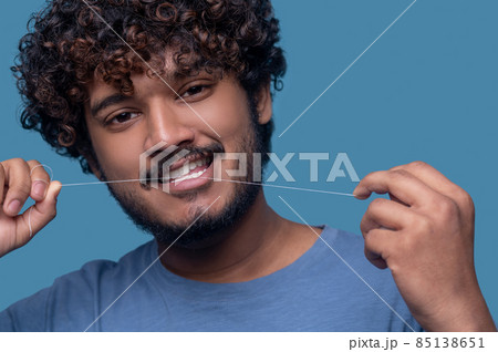 Smiling guy with curly hair flossing his teeth 85138651