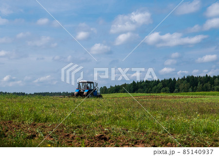Tractor working in the field, plowing the land, preparing for sowing. View of the field and tractor in the distance against a blue sky with clouds 85140937