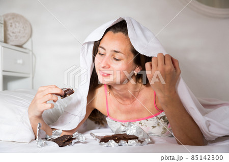 Cute young woman in sleepwear eating chocolate in bed at home 85142300