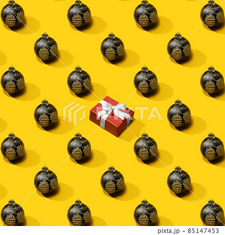 New Year's pattern from black christmas ball decoration with Gift box on yellow background. Christmas pattern made of New Year ball. New Year's pattern from black christmas ball decoration with Gift box on yellow background. Christmas pattern made of New Year ball. 85147453
