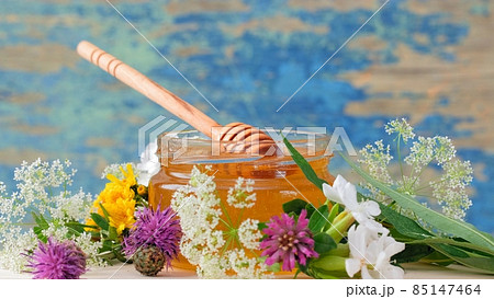 The glass jar with fresh honey on the rustic background. Flowers on the table. 85147464