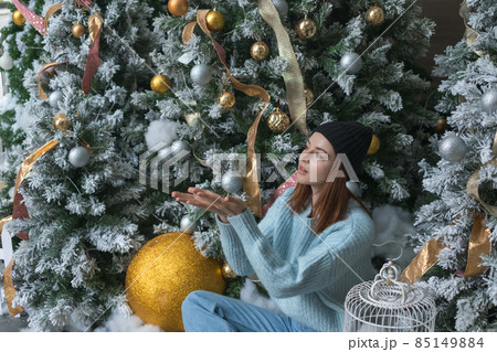 New Year portrait of beautiful caucasian young woman in cozy light blue sweater and hat. Adorable smiling girl sitting near decorated Christmas tree New Year portrait of beautiful caucasian young woman in cozy light blue sweater and hat. Adorable smiling girl sitting near decorated Christmas tree 85149884