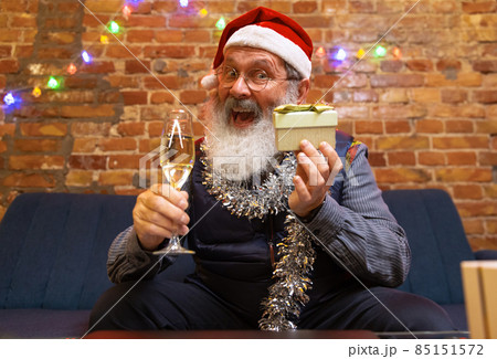 Emotional old bearded man sitting at home and celebrates New Year with friends and family by means of video call. Emotional old bearded man sitting at home and celebrates New Year with friends and family by means of video call. 85151572