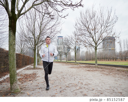 Adult Man running in the parc in winter with city background 85152587