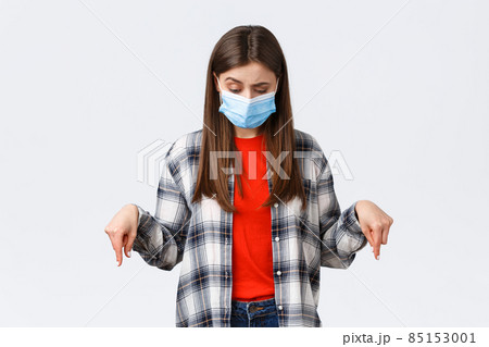 Coronavirus outbreak, leisure on quarantine, social distancing and emotions concept. Hesitant and unsure attractive woman in medical mask, looking down, pointing at strange thing Coronavirus outbreak, leisure on quarantine, social distancing and emotions concept. Hesitant and unsure attractive woman in medical mask, looking down, pointing at strange thing 85153001