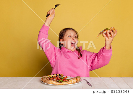 Studio shot of little cute girl sitting and tasting delicious Italian pizza isolated on yellow studio background. Studio shot of little cute girl sitting and tasting delicious Italian pizza isolated on yellow studio background. 85153543