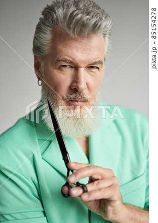 Portrait of brutal middle aged man with beard looking at camera, posing with sharp barber scissors over white background 85154278
