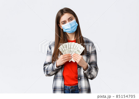 Money transfer, investment, covid-19 pandemic and working from home concept. Pleased young female employee, freelancer in medical mask holding her salary or won cash, white background 85154705