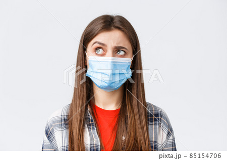 Coronavirus outbreak, leisure on quarantine, social distancing and emotions concept. Intrigued and hesitant young woman in medical mask, looking upper left corner reluctant, white background 85154706