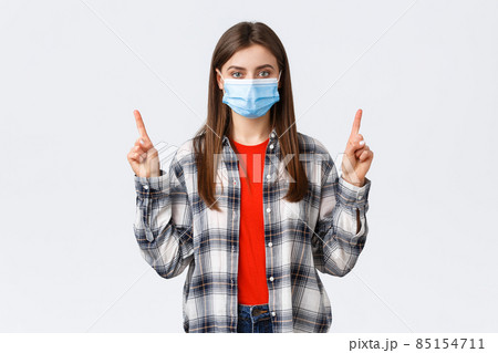 Coronavirus outbreak, leisure on quarantine, social distancing and emotions concept. Confident and determined young woman self-isolating home, pointing fingers up, wear medical mask 85154711