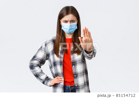 Coronavirus outbreak, leisure on quarantine, social distancing and emotions concept. Young woman in medical mask look disappointed, disapprove smth, show stop or prohibition gesture 85154712