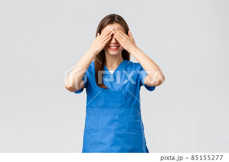 Healthcare workers, prevent virus, insurance and medicine concept. Young optimistic female nurse, doctor in scrubs, shut eyes with hands and smiling, anticipating surprise, being blindfolded 85155277