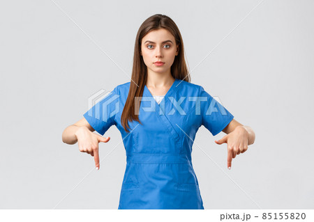 Healthcare workers, prevent virus, covid-19 test screening, medicine concept. Serious professional physician, doctor or nurse in blue scrubs, pointing fingers down, provide coronavirus information Healthcare workers, prevent virus, covid-19 test screening, medicine concept. Serious professional physician, doctor or nurse in blue scrubs, pointing fingers down, provide coronavirus information 85155820